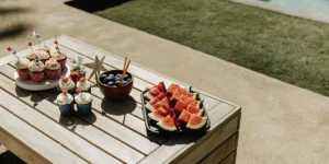 Cupcakes and fruit bowls with watermelon slices arranged on a poolside picnic table