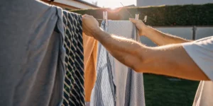 man hanging freshly washed clothes on an outdoor clothesline at sunset