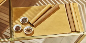 Aerial view of brown paper rolls, small bowls of ingredients, and chocolate wraps on a golden mat.
