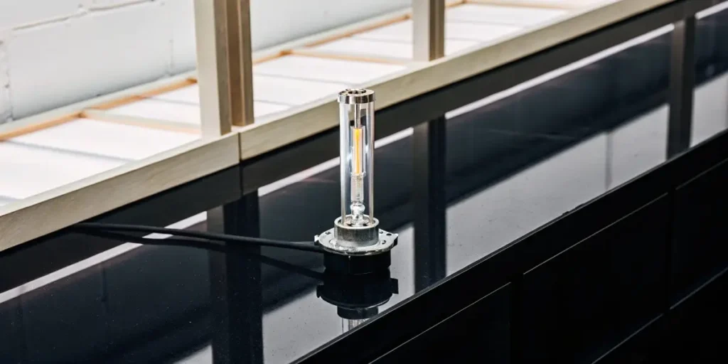 A silver, rectangular HID lamp ballast connected by a green cable, placed on wood in a workshop.