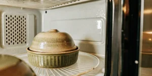 Macro photograph of a two-toned ceramic pot with a lid, sitting on a rack inside an open microwave.
