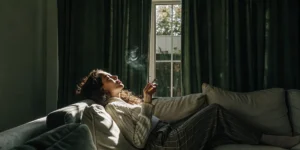 Woman relaxing on sofa smoking cannabis joint in dimly lit room
